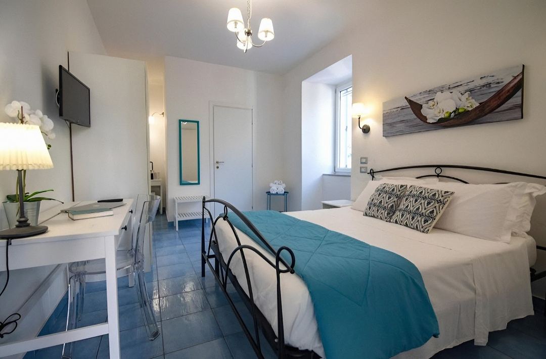 A bright, modern bedroom with a queen bed, teal accents, desk workspace, and nautical-themed wall art at Sonnino B&B.