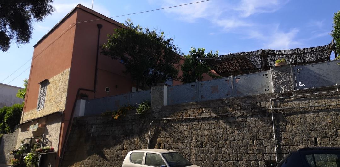 The terracotta-colored exterior of Sonnino B&B with stone walls and parked vehicles in front.